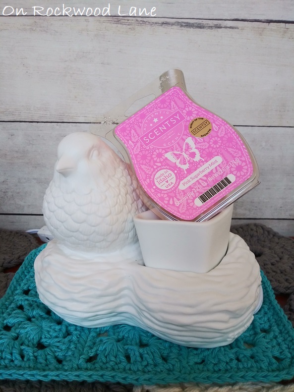 Birds of a Feather Wax Warmer shown on top of the blue doily with the March scent of the month wax, Pink Sugarberry Mint.